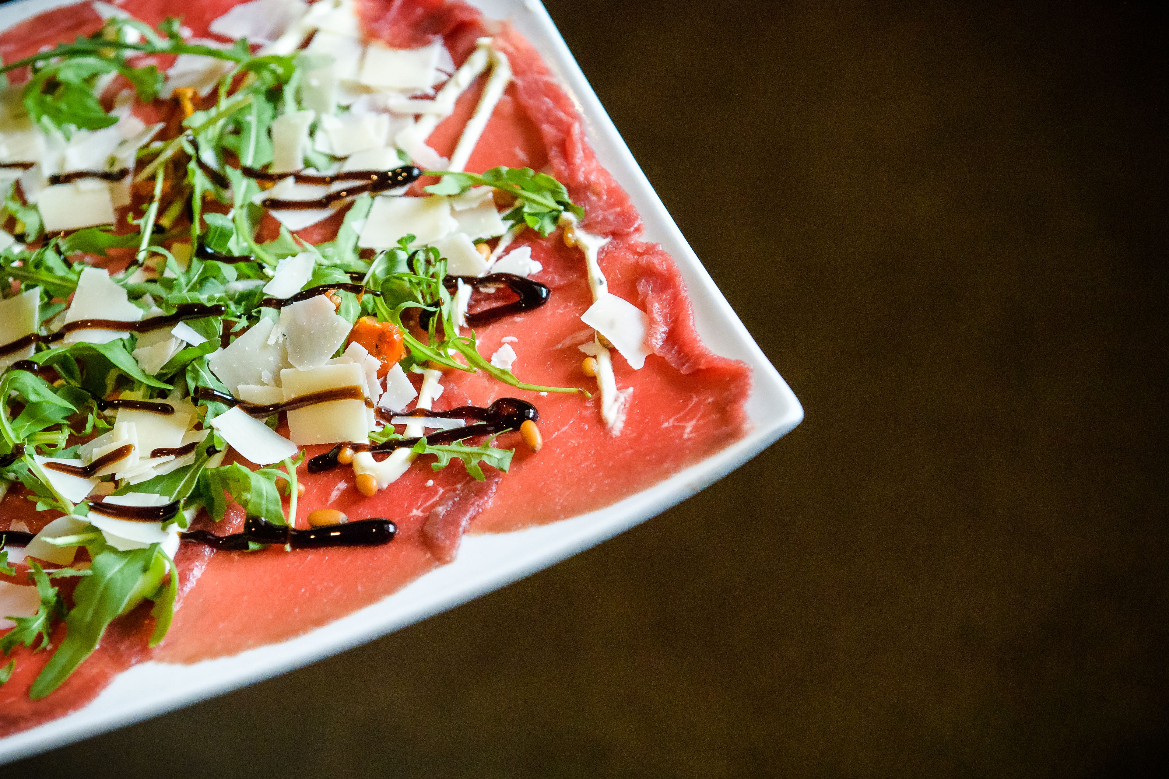 A rectangular plate with a pinkish food item, garnished with greens, cheese, and a drizzle of sauce.