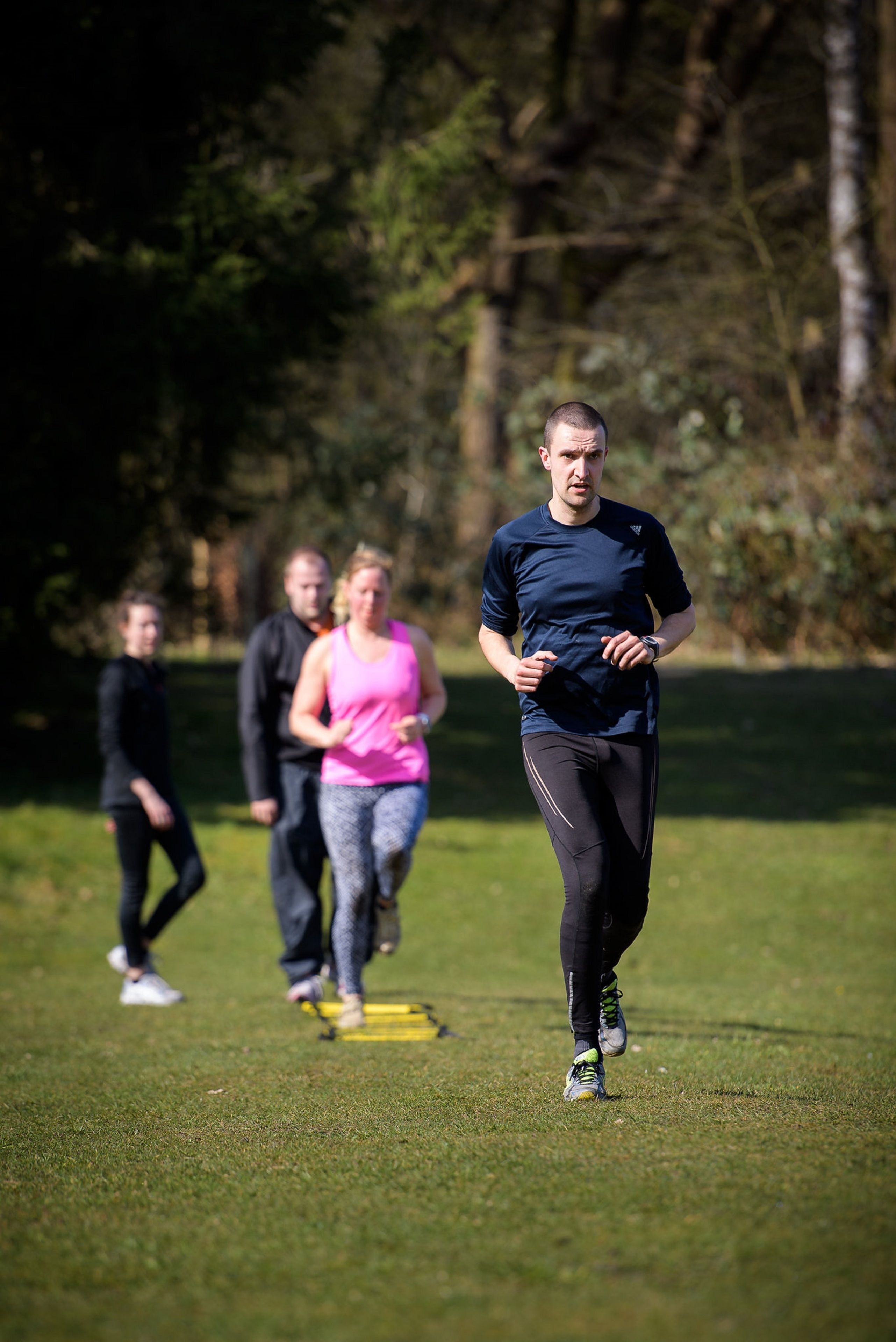 A group of people jogging on a grassy field with trees in the background.
