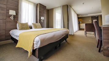 Una habitación de hotel con una cama grande, dos mesitas de noche, un escritorio y una silla.