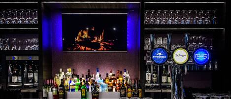 A bar with a fireplace, shelves of bottles, and a selection of glasses.