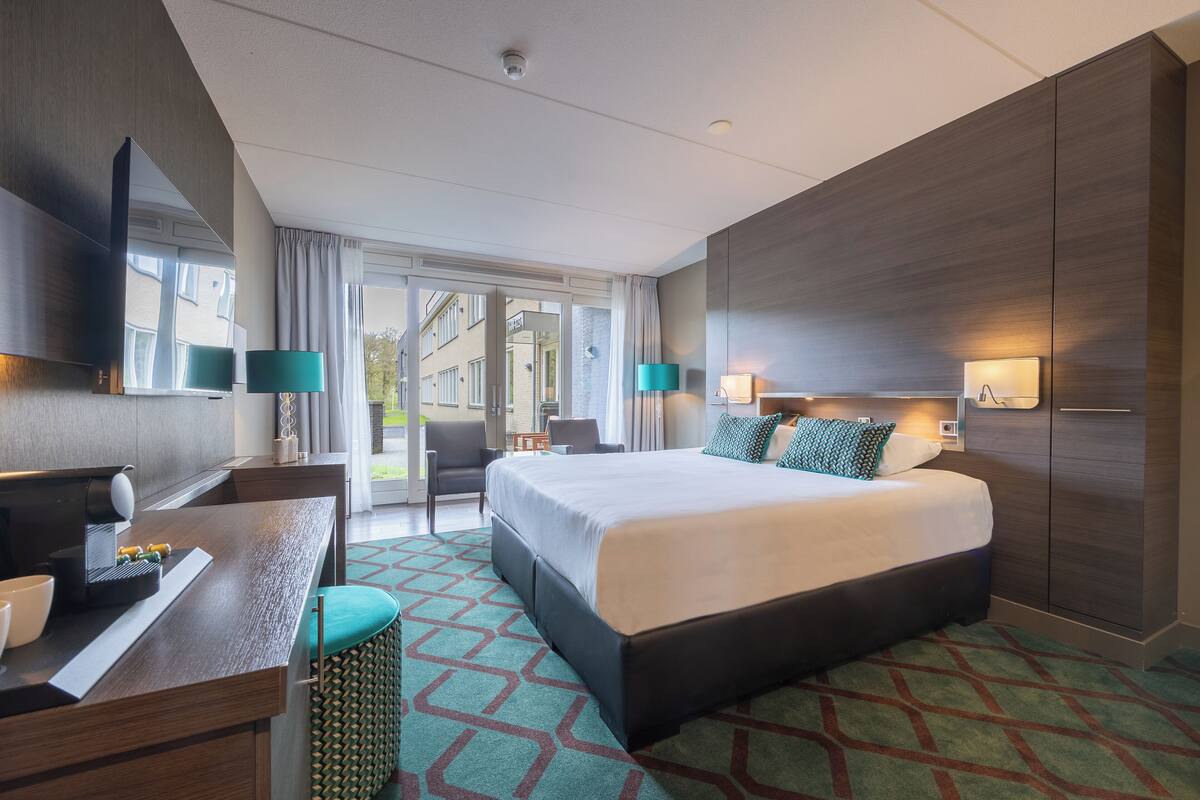 Une chambre d’hôtel moderne dotée d’un grand lit, d’un bureau avec une chaise, d’une télévision et d’une fenêtre avec des rideaux.