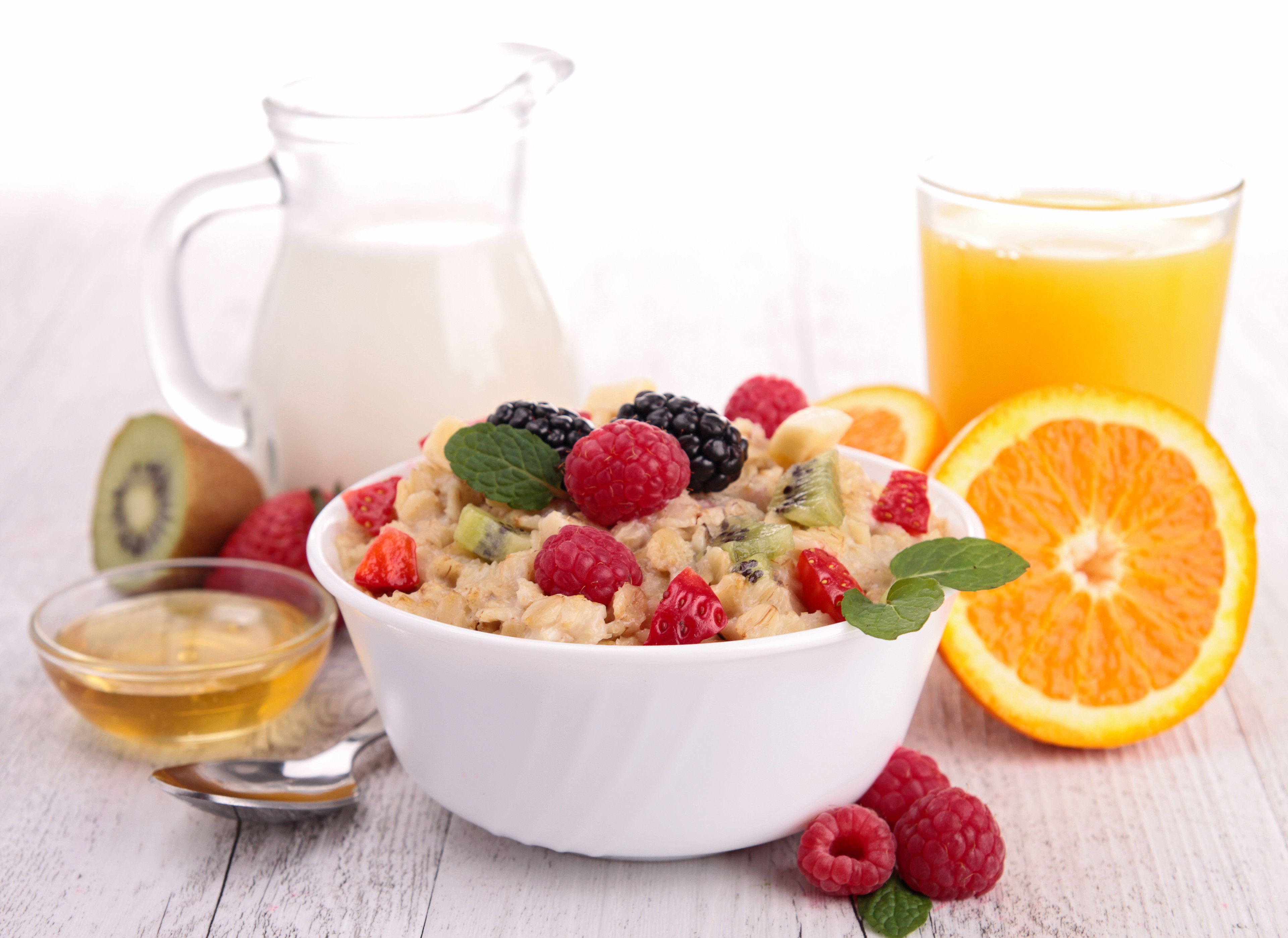 Un tazón de cereal con frutas, un vaso de jugo de naranja, una jarra de leche y un recipiente pequeño de miel.