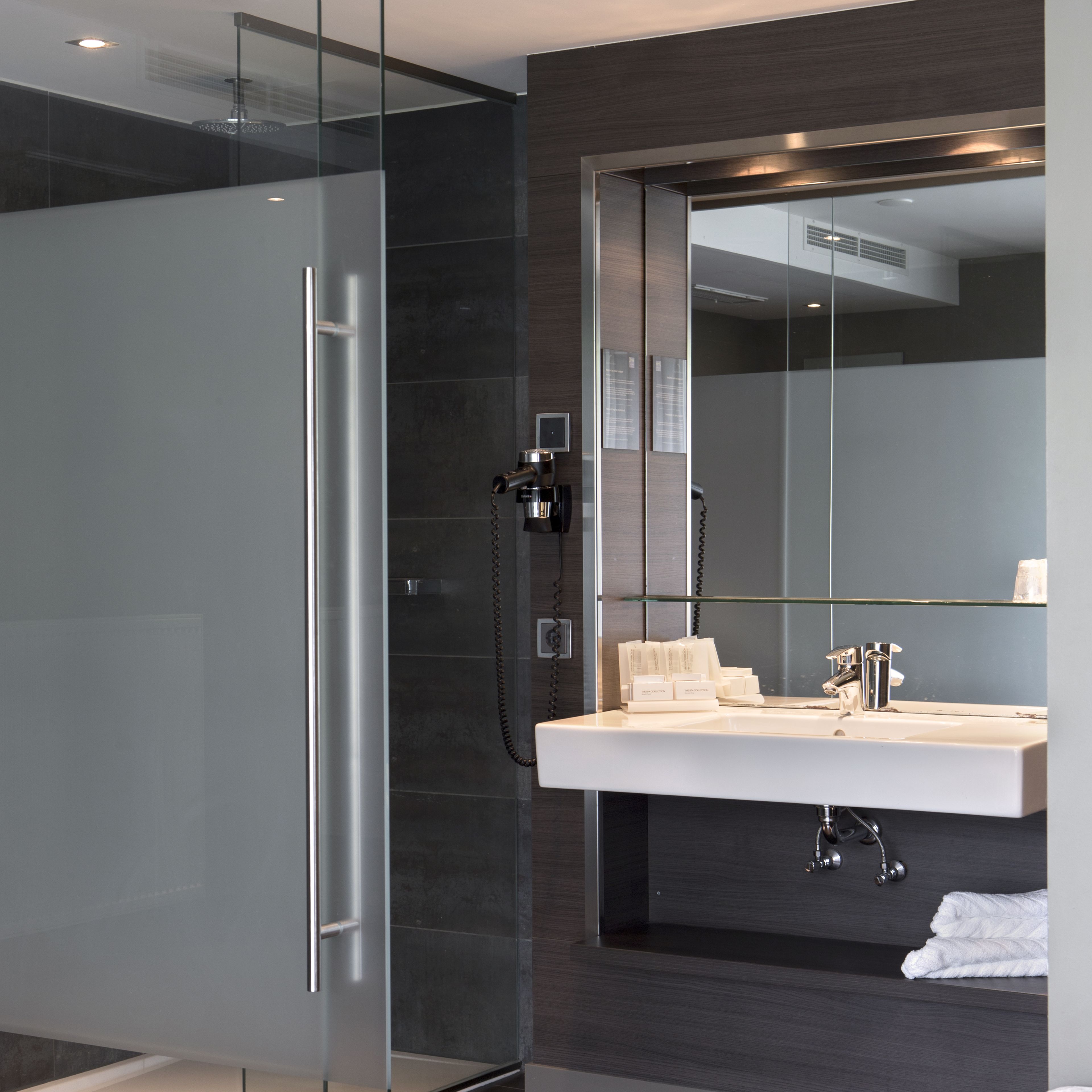 A modern bathroom with a glass-enclosed shower, a large mirror, and a white sink with a towel.