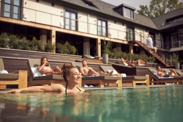 A pool area with lounge chairs and a building in the background. - Van der Valk Hotel Gilze - Tilburg (Gilze)