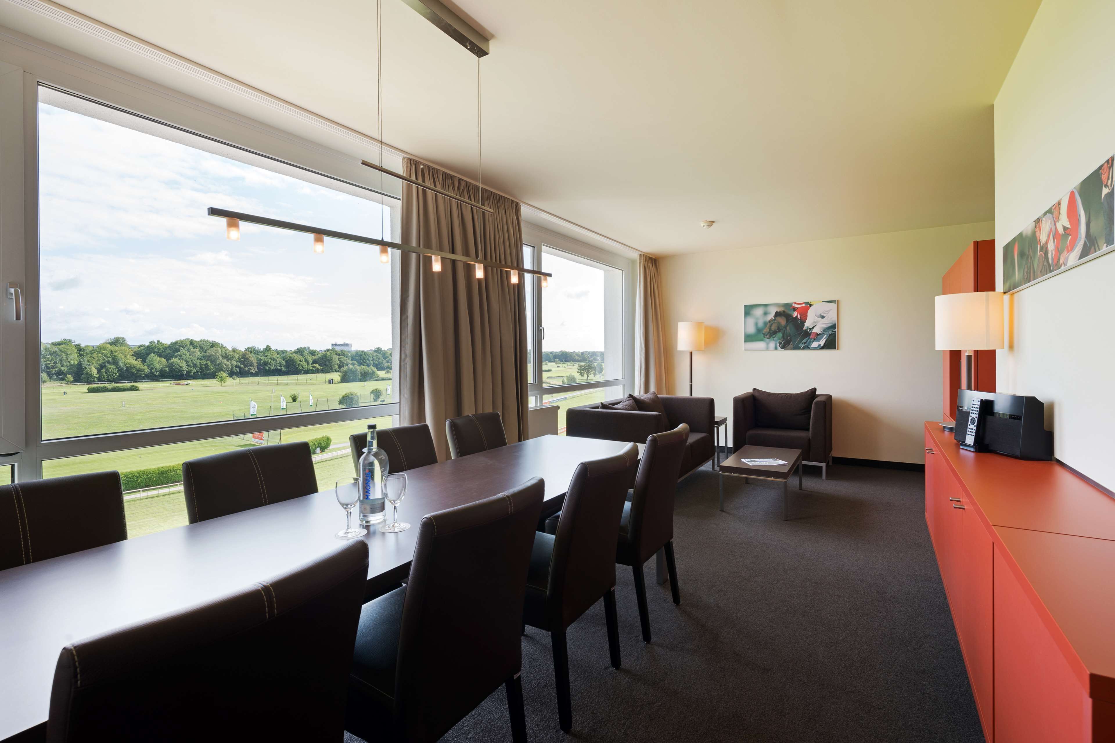 Et hotelværelse med spiseplads, en sofa og udsigt over et grønt landskab.