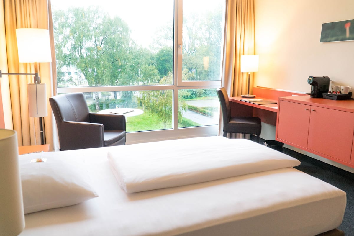 Habitación de hotel con cama, escritorio, silla y vistas a zonas verdes.