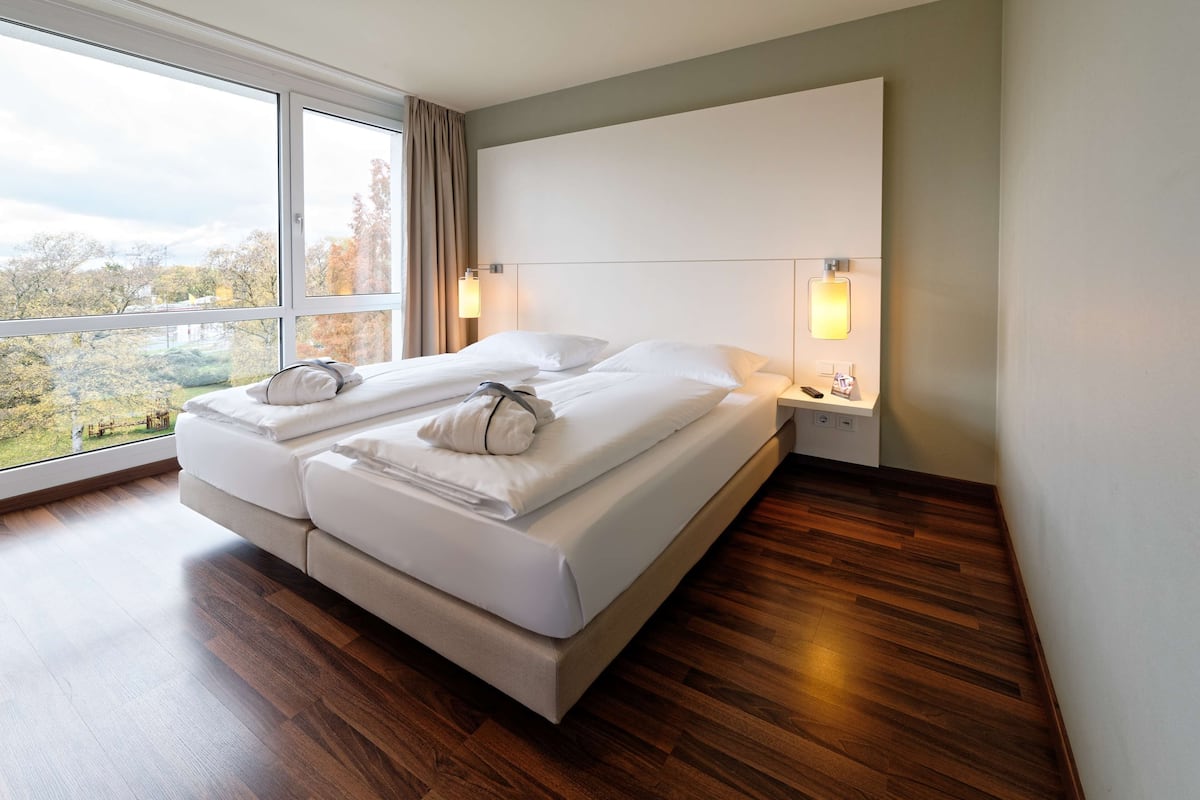 Habitación de hotel moderna con una cama grande, suelo de madera y vistas al exterior.