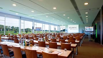 A conference room with multiple tables and chairs, large windows, and a presentation screen.