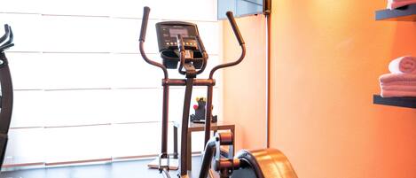 Un gimnasio con equipo de ejercicio, un televisor en la pared y toallas en un estante.