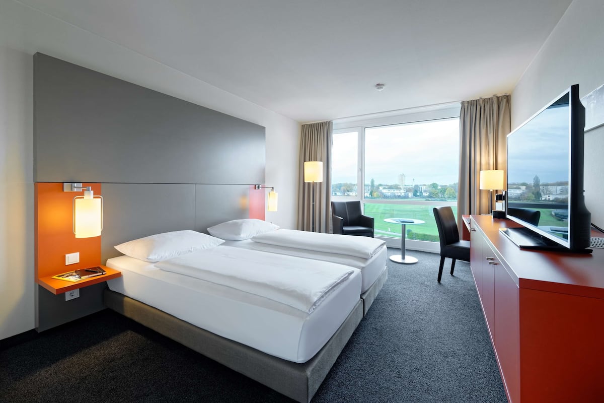 Habitación de hotel con dos camas, un escritorio, un televisor y vista a la ciudad.