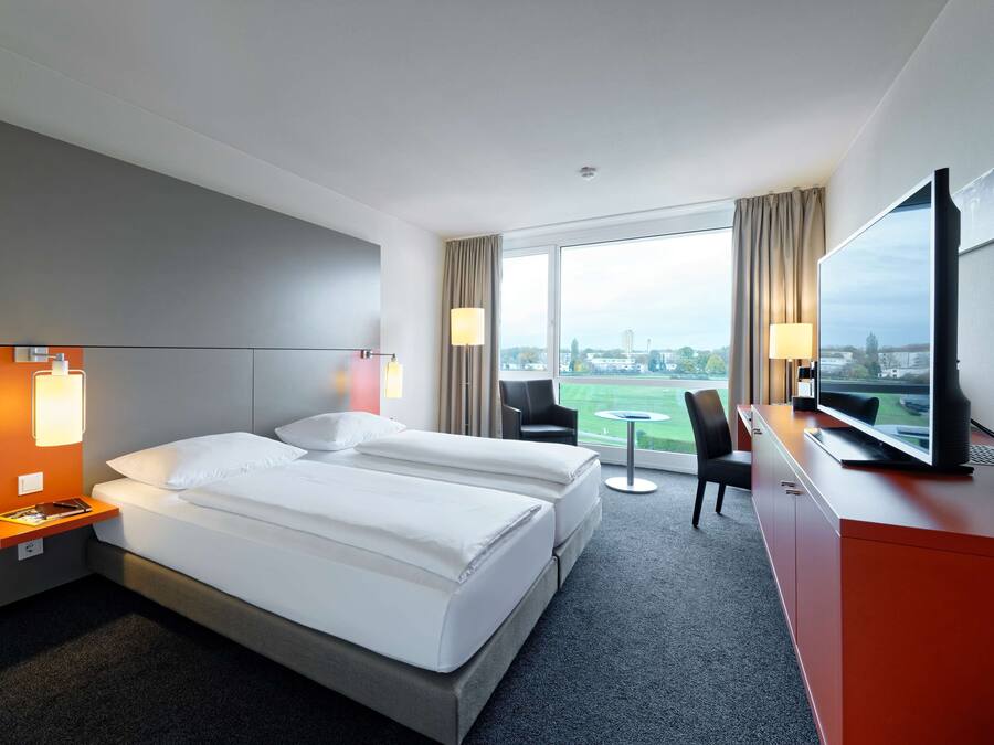 Quarto de hotel com duas camas, uma escrivaninha, televisão e vista para a cidade.
