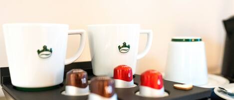 Una bandeja con tres tazas blancas, cada una con el logotipo de una corona verde, y tres pequeños dulces bañados en chocolate.