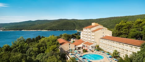 Un resort con una piscina grande, varias edificaciones y vistas al mar y a las colinas.