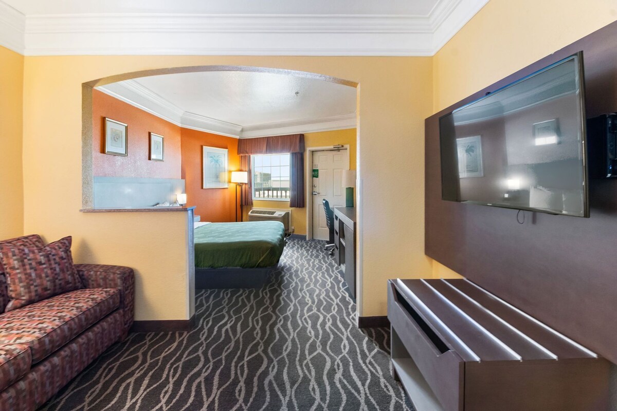 A hotel room with a sofa, a bed, a TV, and a hallway leading to another room.