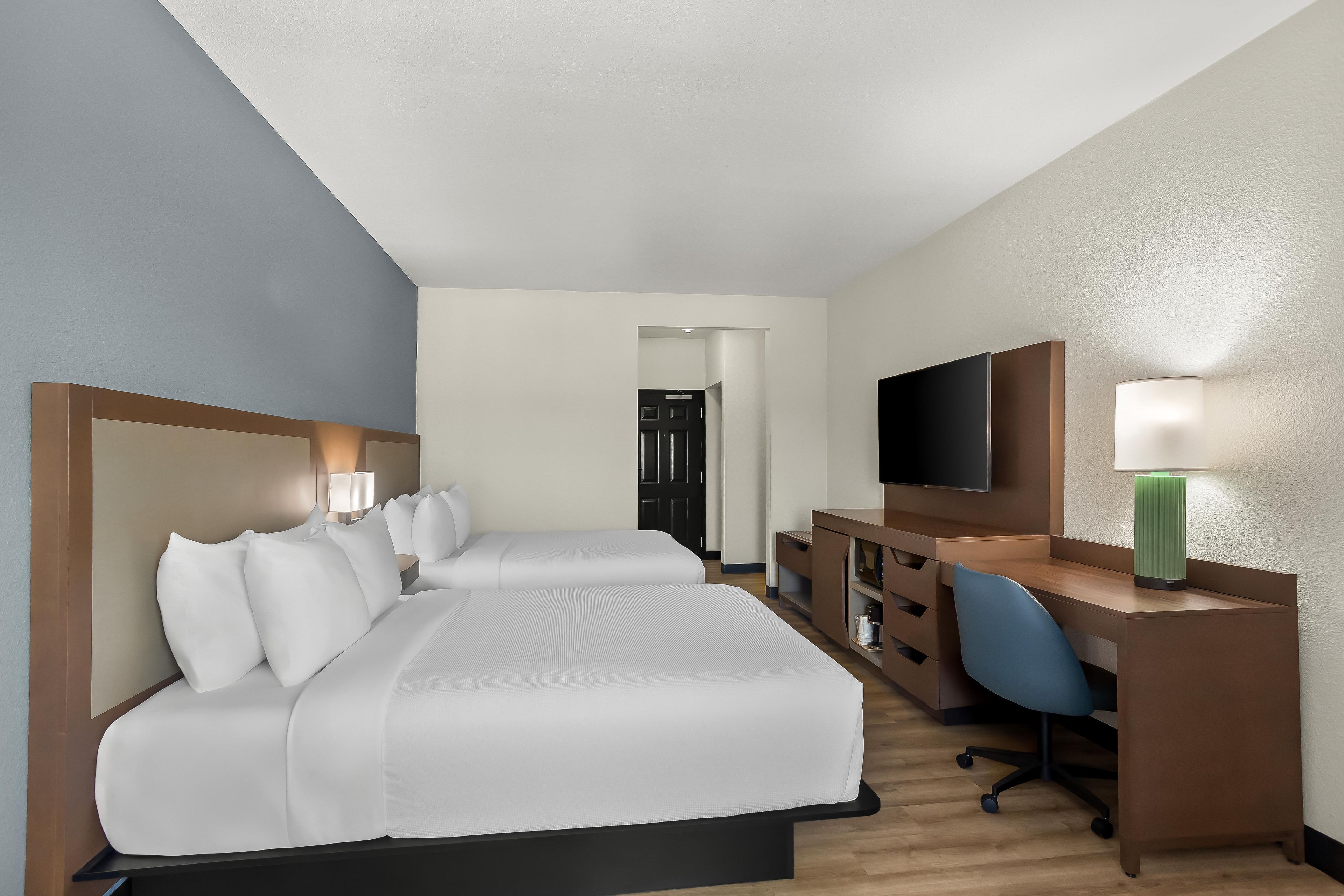 A hotel room with two beds, a desk with a chair, a television, and a lamp.