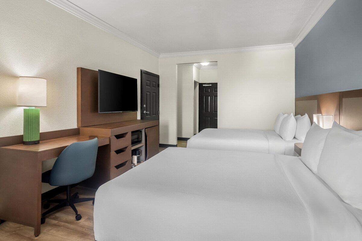 A hotel room with a bed, a desk, a chair, a television, and a door.