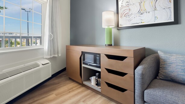 Ein modernes Zimmer mit Fenster, einer Wandleuchte, einer Mikrowelle und einem Sofa.