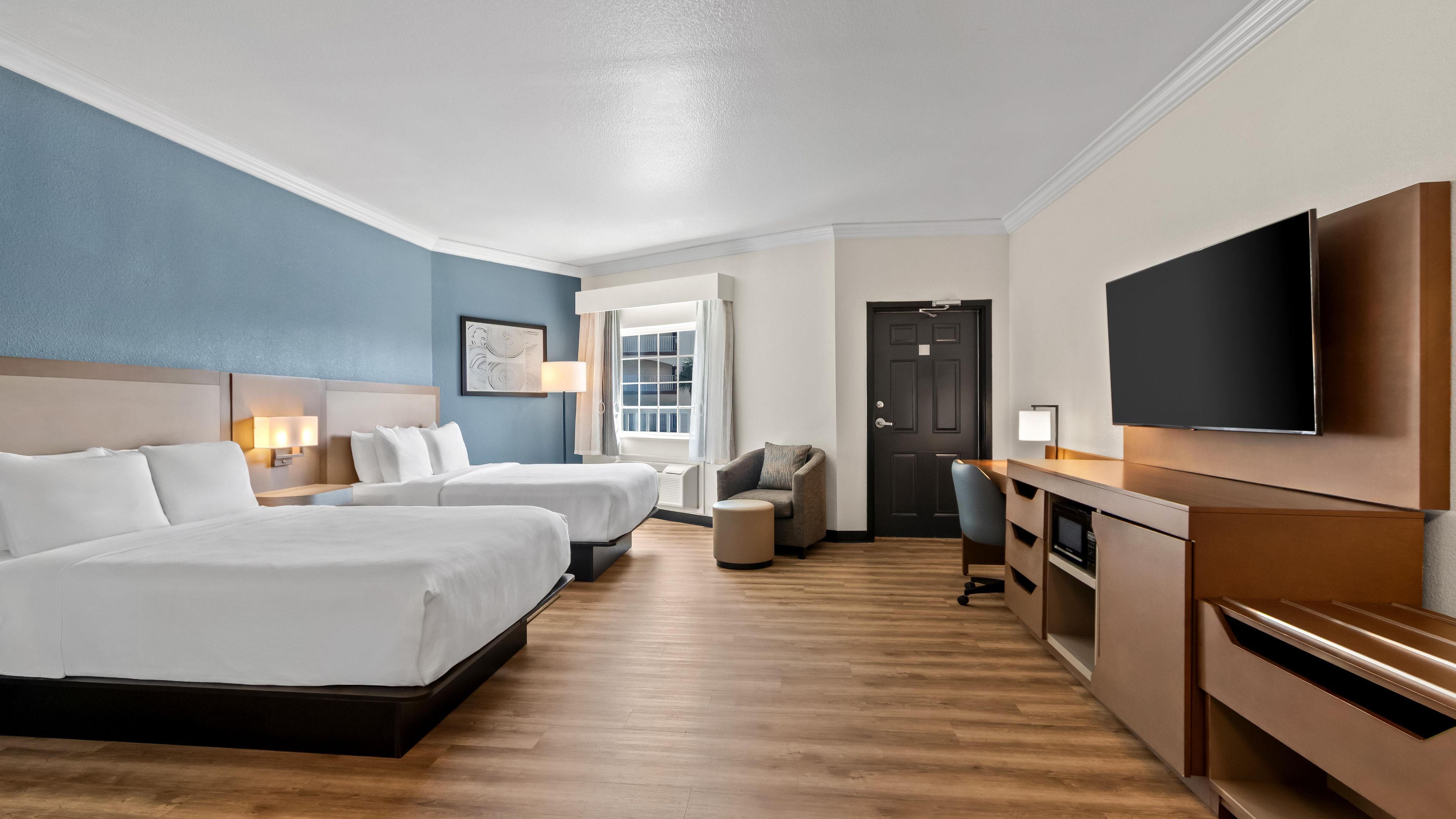 Ein Hotelzimmer mit zwei Betten, einem Schreibtisch, einem Fernseher und einem Fenster mit Vorhängen.