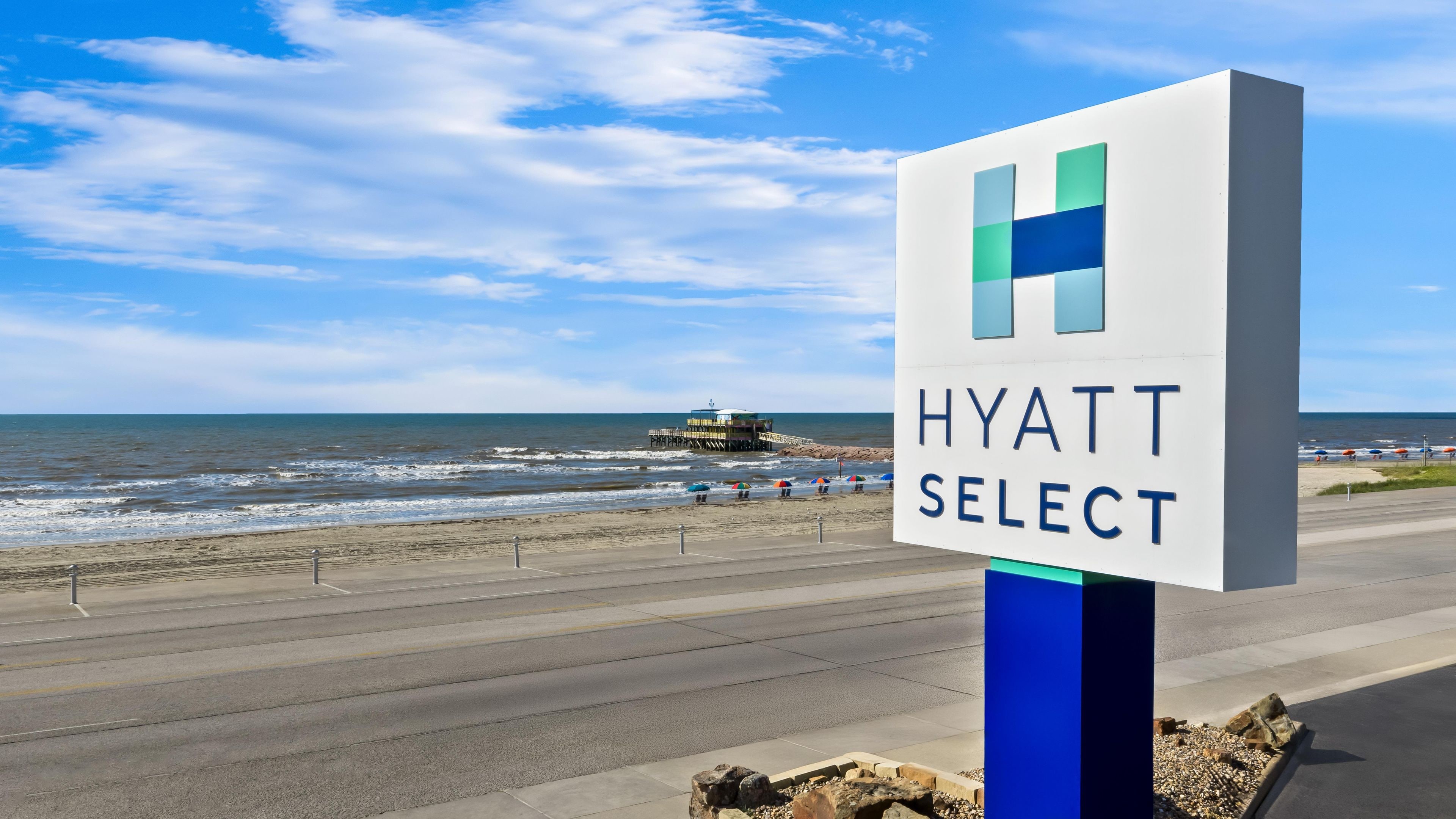 Skilt for 'Hyatt Select' med udsigt til stranden og havet i baggrunden.