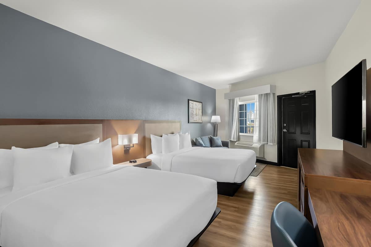 Quarto de hotel com duas camas, uma escrivaninha, televisão e janela com cortinas.