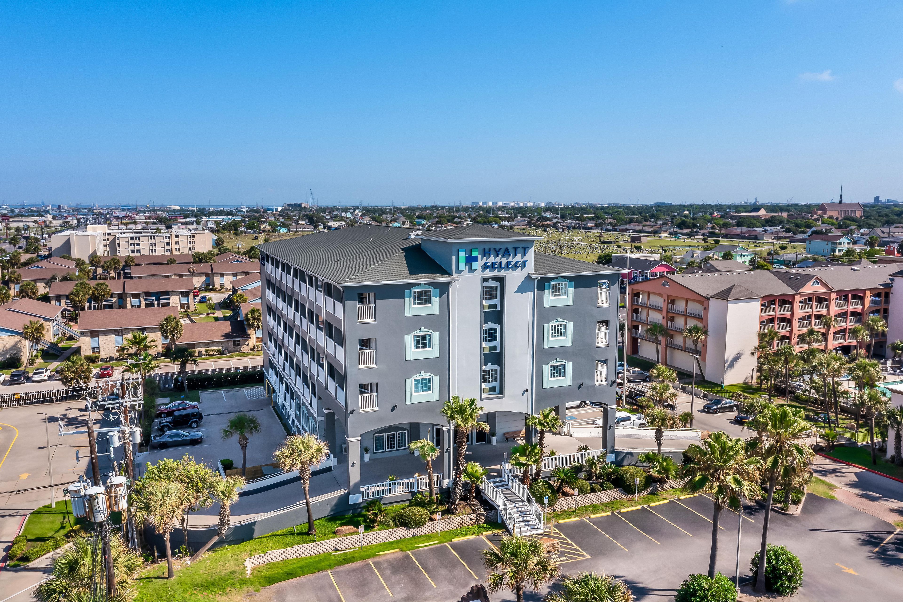 A multi-story hotel with a modern design, featuring a prominent sign, a parking lot, and surrounding greenery.