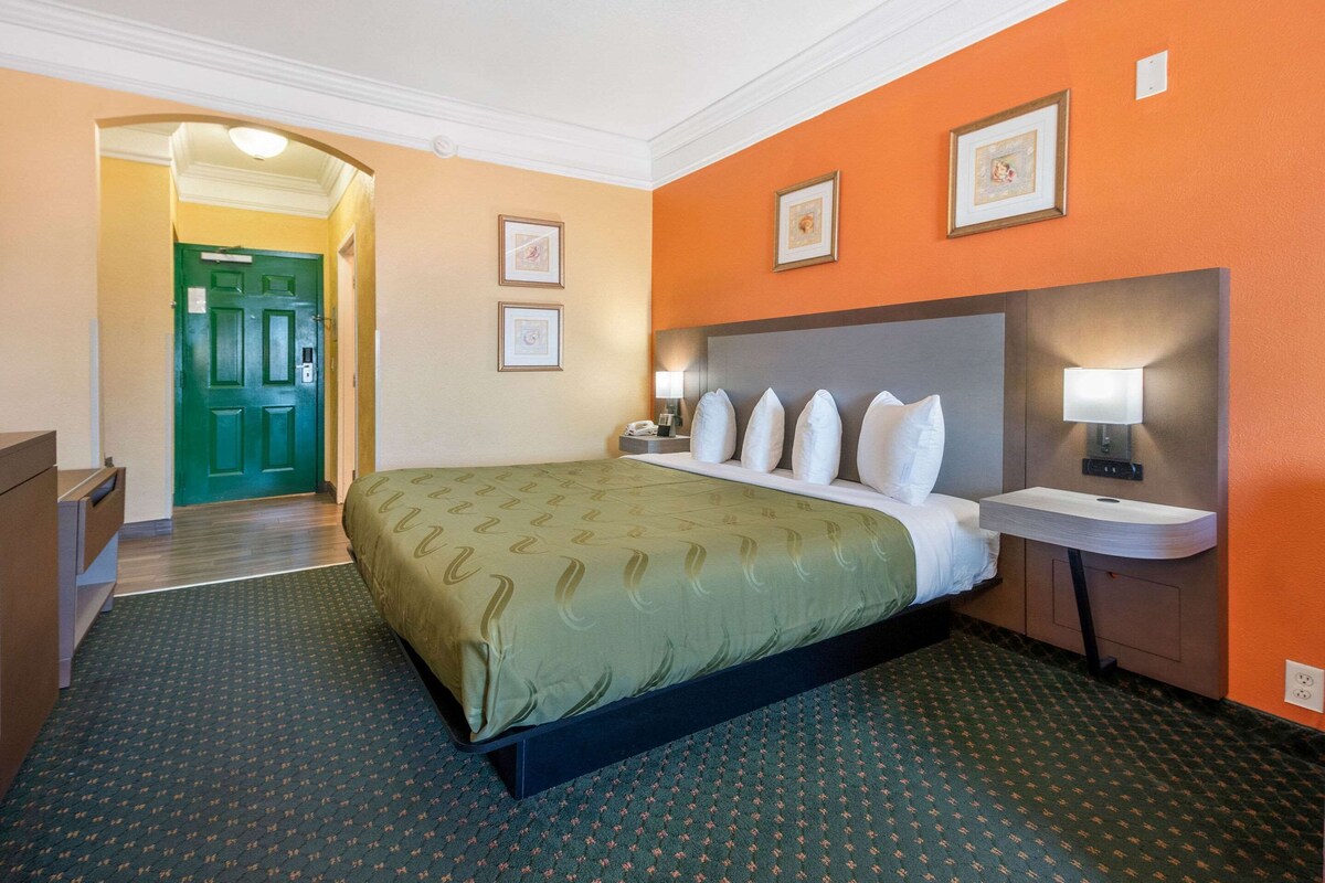 A hotel room with a bed, bedside table, lamp, and framed pictures on the wall.