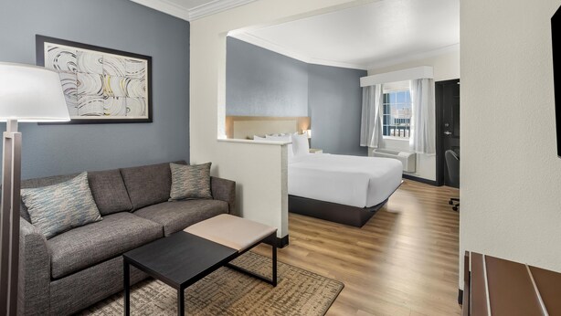 A hotel room with a sofa, a small table, a bed, a nightstand, and a painting on the wall. - Hyatt Select Galveston - Beachfront (Galveston)