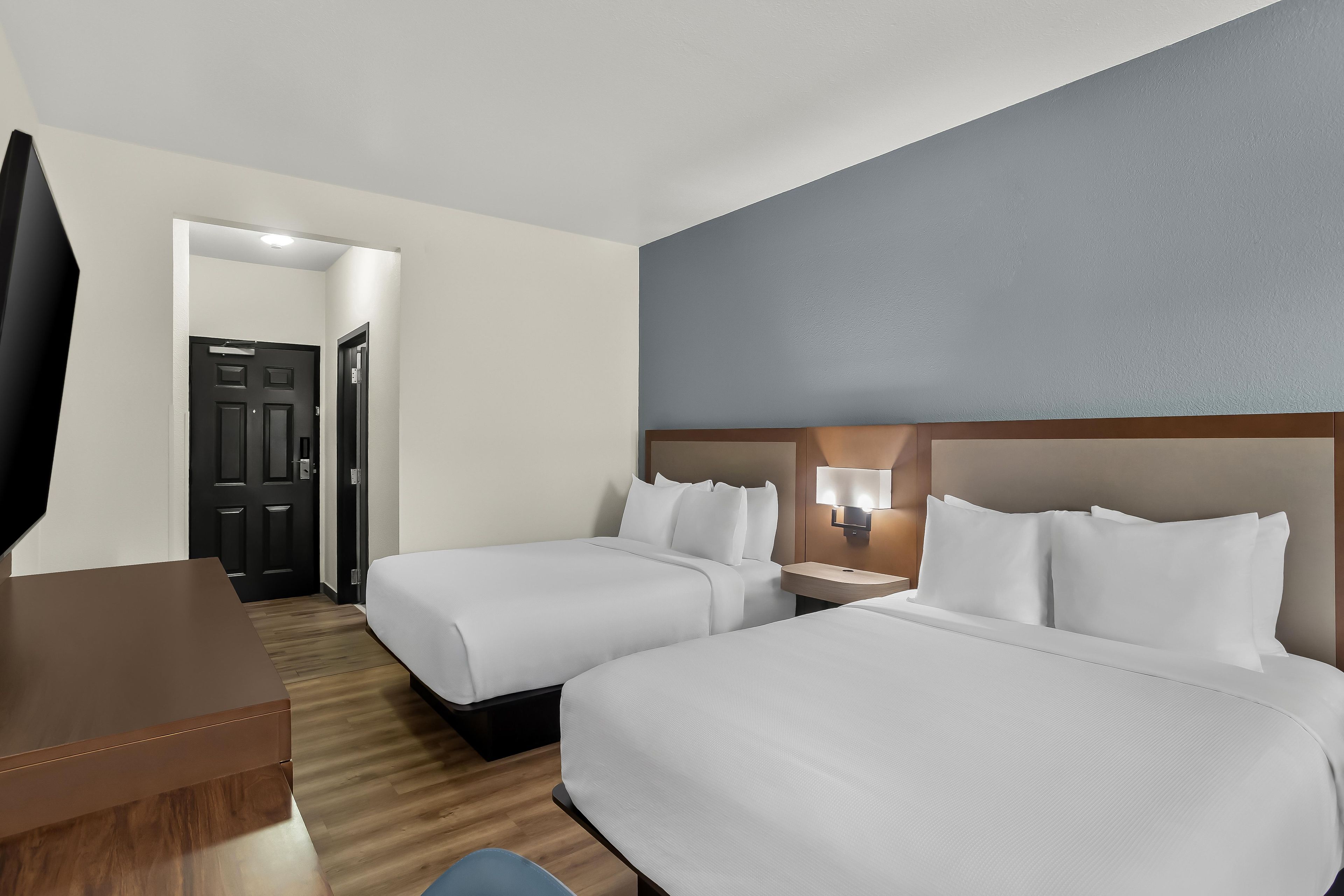Una habitación de hotel con dos camas, un escritorio, una silla, un televisor y una puerta.