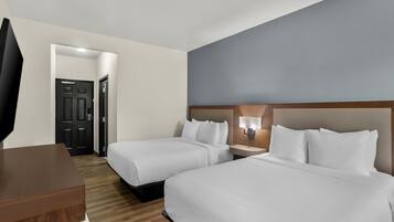 Una habitación de hotel con dos camas, un escritorio, una silla, un televisor y una puerta.
