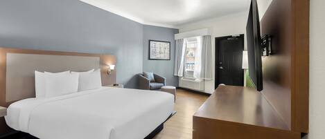 A hotel room with a large bed, a desk, a chair, a TV, and a window with curtains.