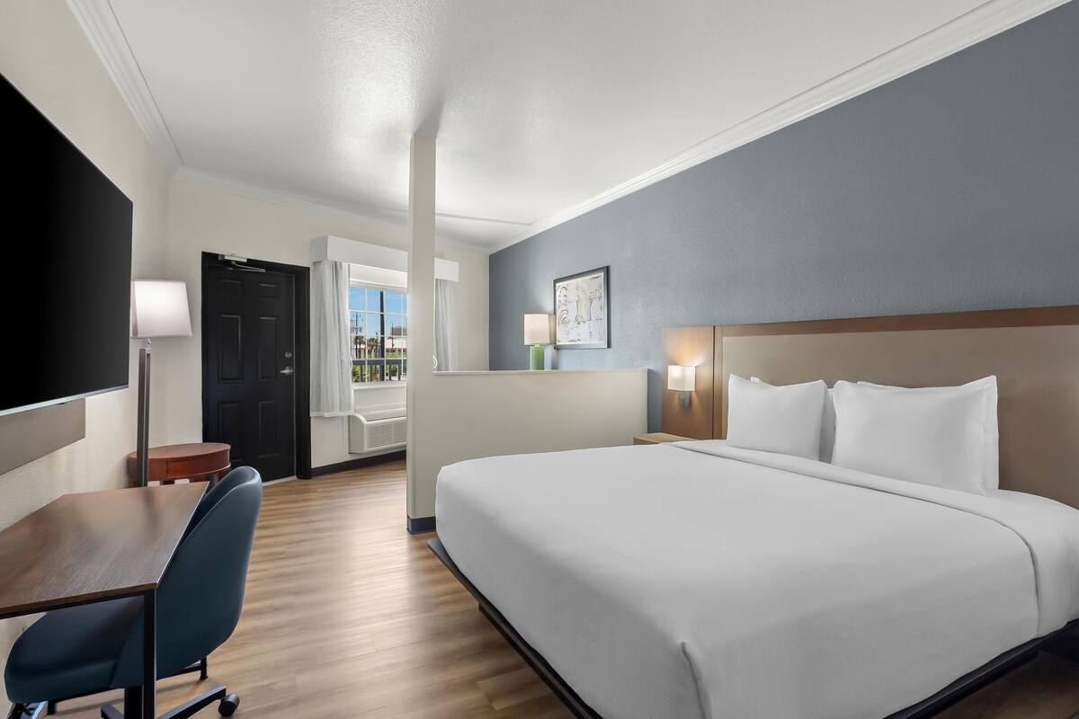 Quarto de hotel com cama, escrivaninha, cadeira e vista para o exterior.