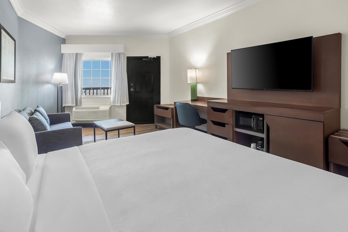 Quarto de hotel com uma cama grande, uma escrivaninha, uma cadeira, uma televisão e uma janela com cortinas.