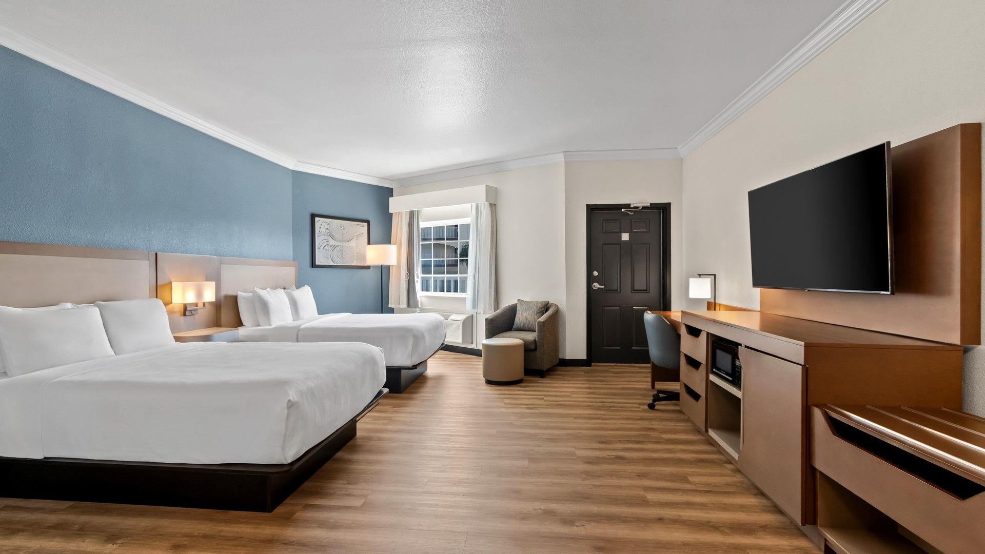 A hotel room with two beds, a desk, a chair, a television, and a window with curtains.