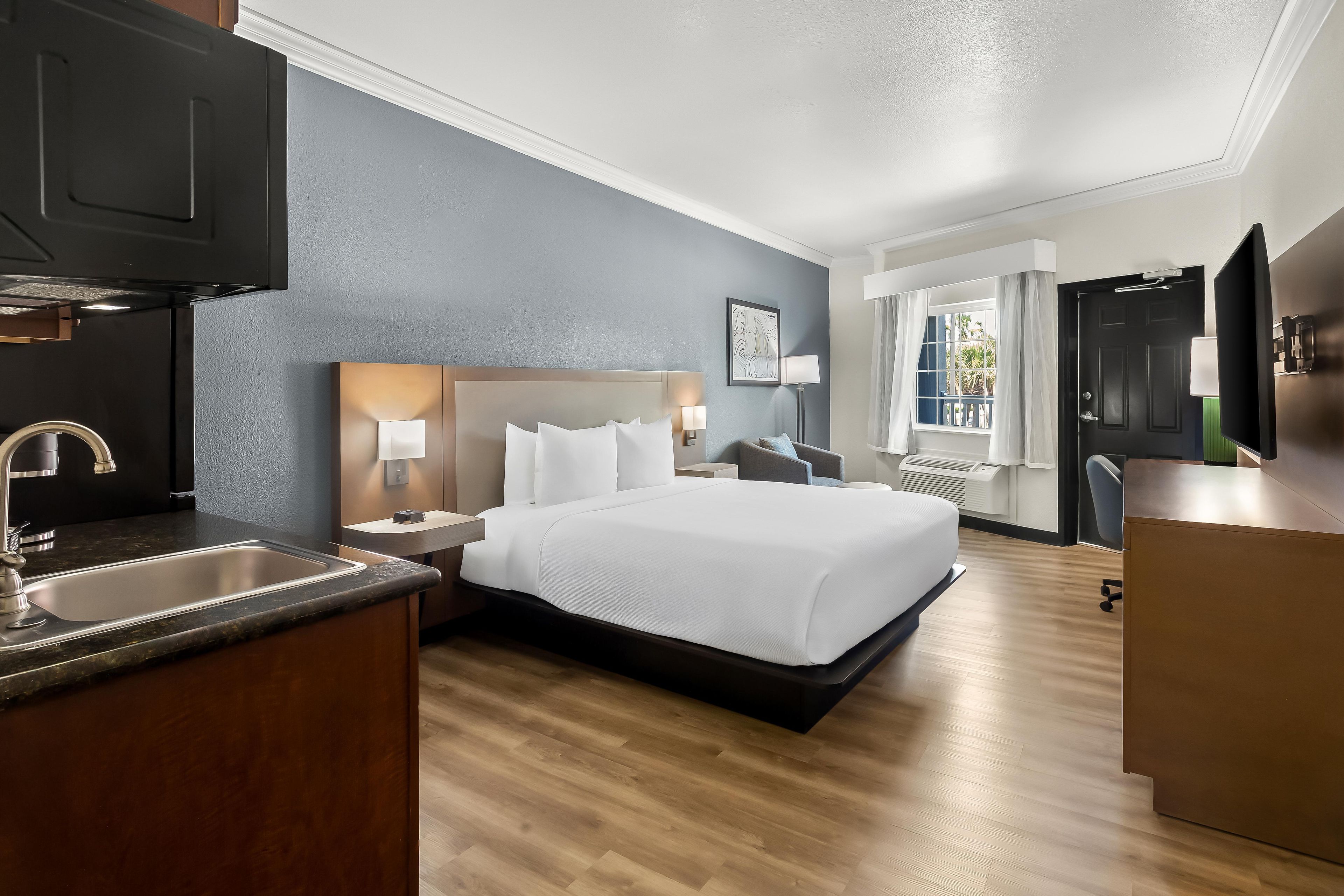 Habitación de hotel con cama, escritorio, televisor, ventana con cortinas, lavabo y armario.