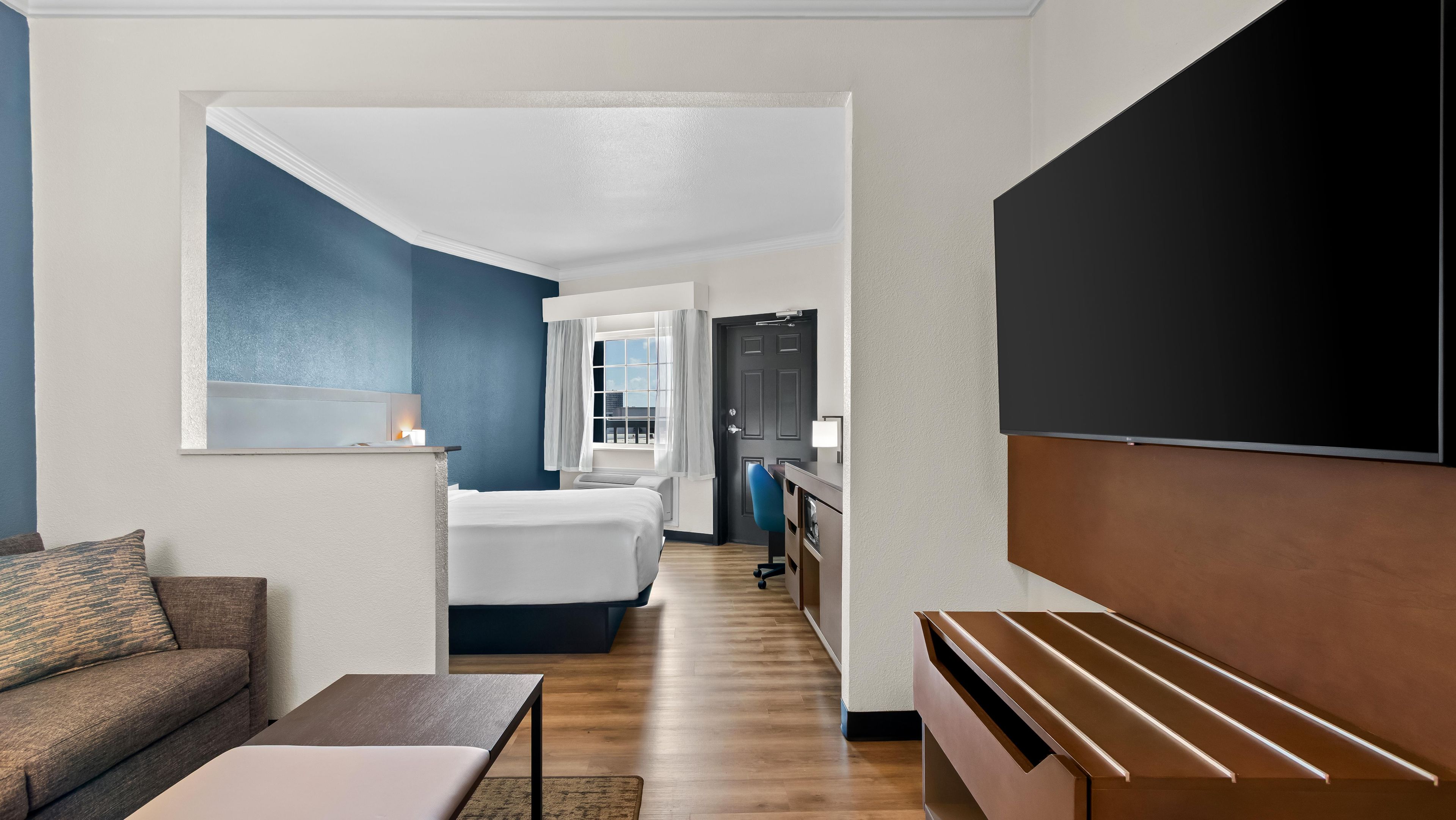 A hotel room with a bed, a desk, a TV, and a view of the city.