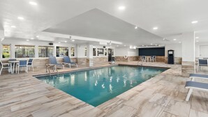 An indoor swimming pool with tiled flooring, lounge chairs, and a seating area with tables and chairs. - Hyatt Select Galveston - Beachfront (Galveston)