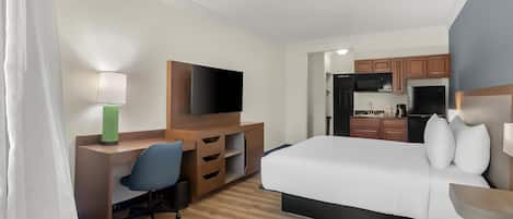 Habitación de hotel con cama, escritorio, silla, televisor y kitchenette.