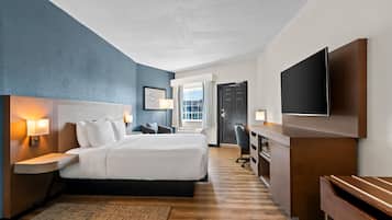Een hotelkamer met een groot bed, nachtkastjes met lampen, een bureau met een flatscreen-tv en uitzicht op het omliggende landschap door een raam.