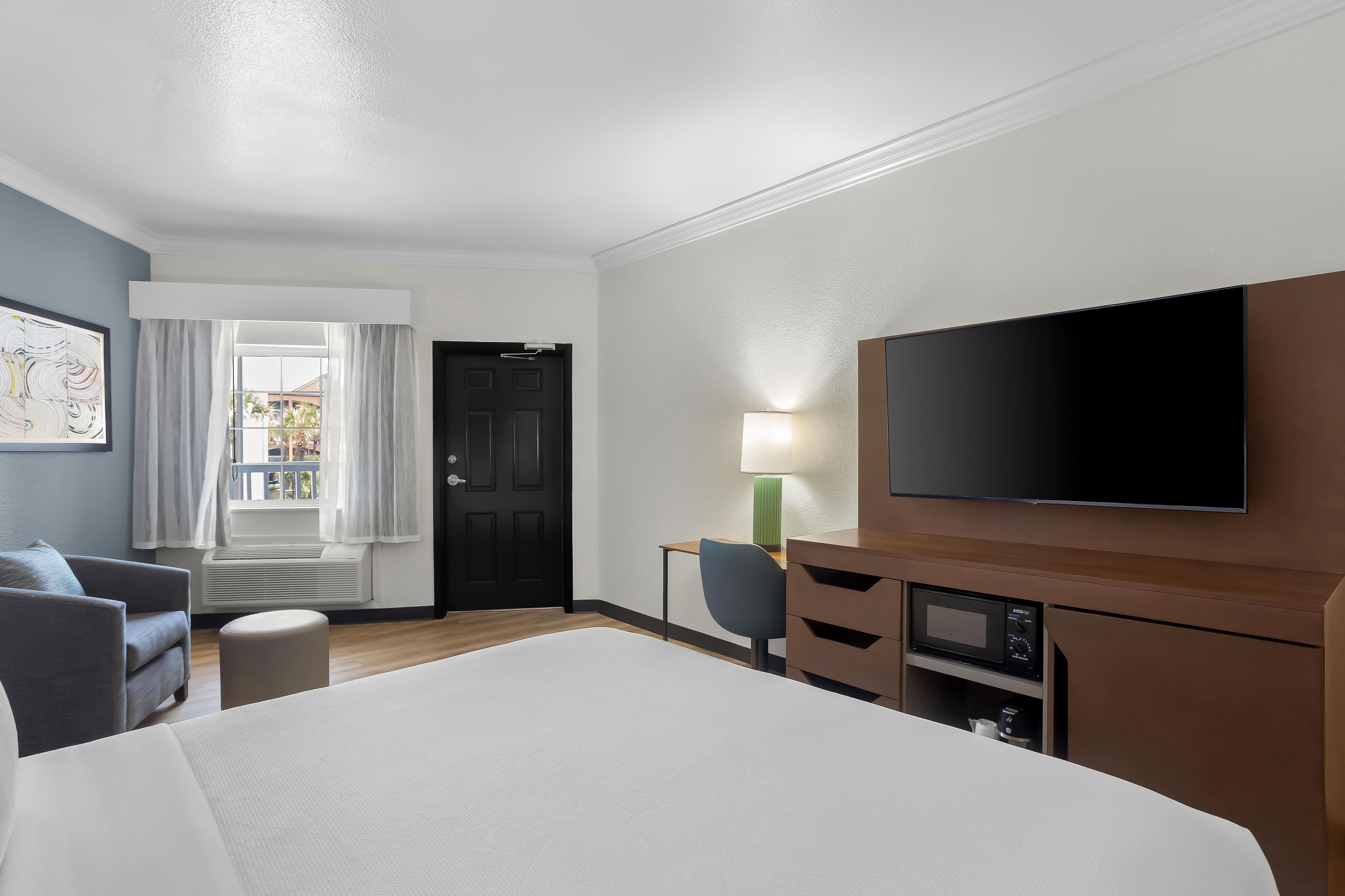 A hotel room with a bed, a desk, a chair, a television, and a window with curtains.