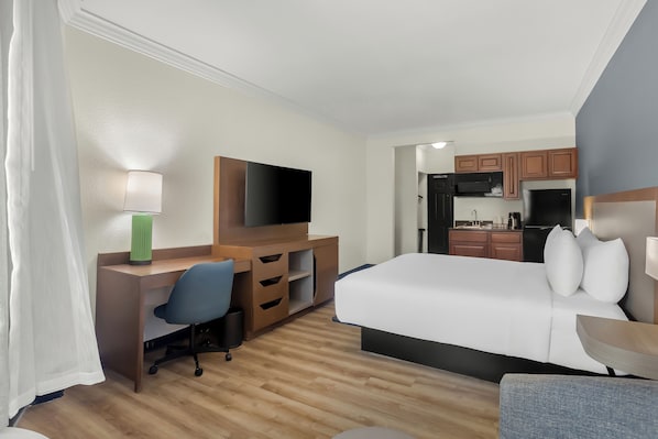 Habitación de hotel con cama, escritorio, silla, televisor y kitchenette.