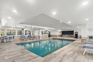 Une piscine intérieure avec un sol carrelé, des chaises longues et un espace détente comprenant des tables et des chaises.
