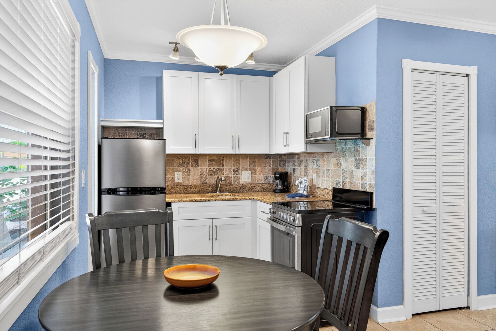 A kitchen with white cabinets, a stainless steel refrigerator, a microwave, and a tiled backsplash.