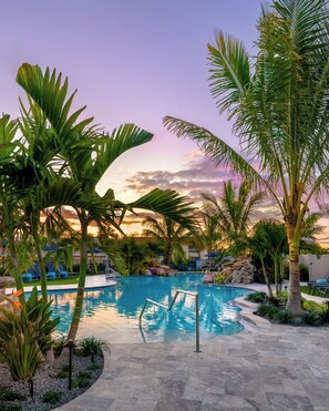 A pool area with palm trees, lounge chairs, and a stone pathway.