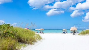 A beach with white sand, clear blue water, and a few beach umbrellas. - Tropical Beach Resorts (Siesta Key)