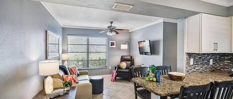 A modern kitchen with granite countertops, a dining area with black chairs, and a ceiling fan.