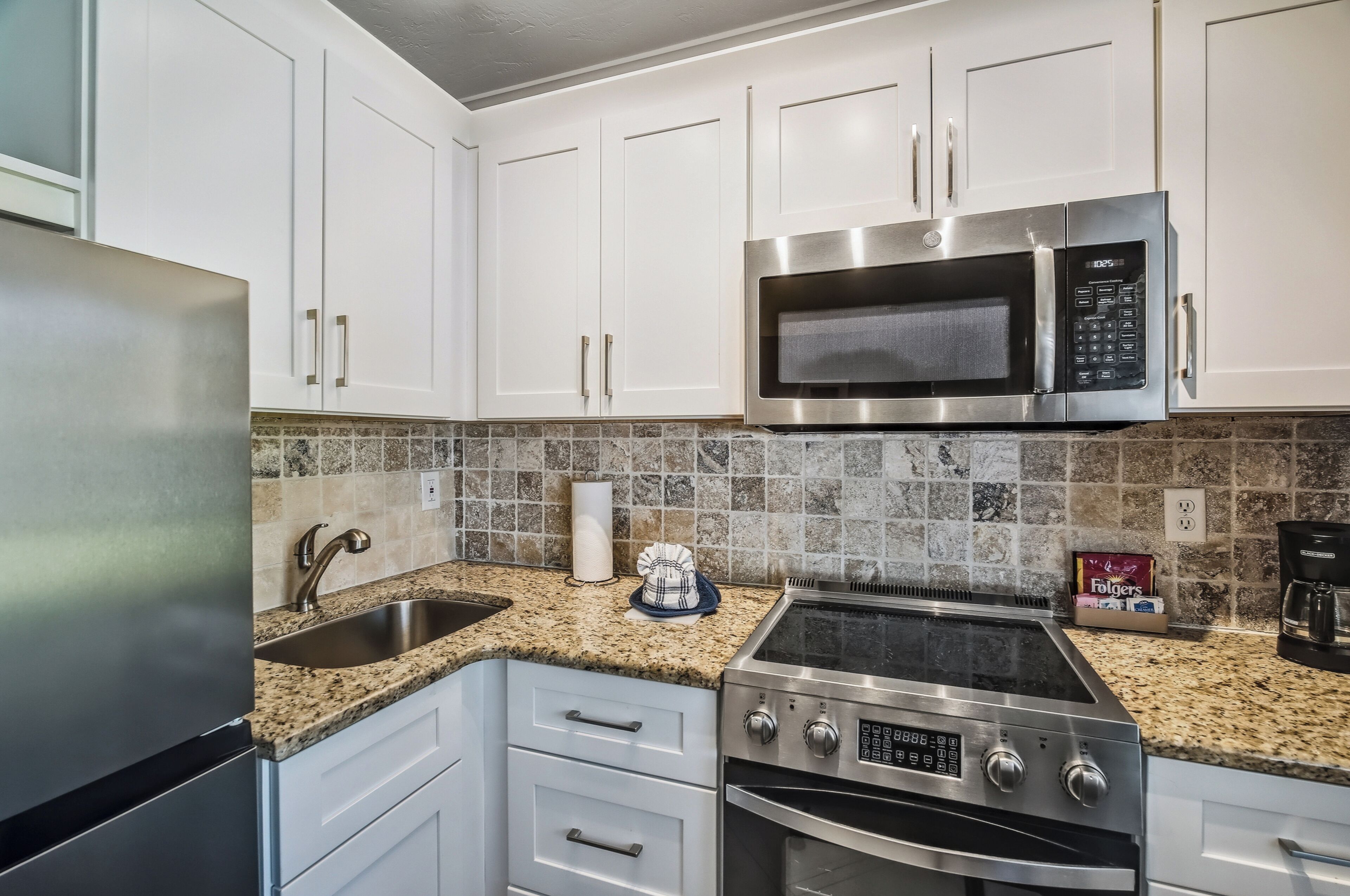 A kitchen with white cabinets, a stainless steel microwave, a gas stove, and a granite countertop.