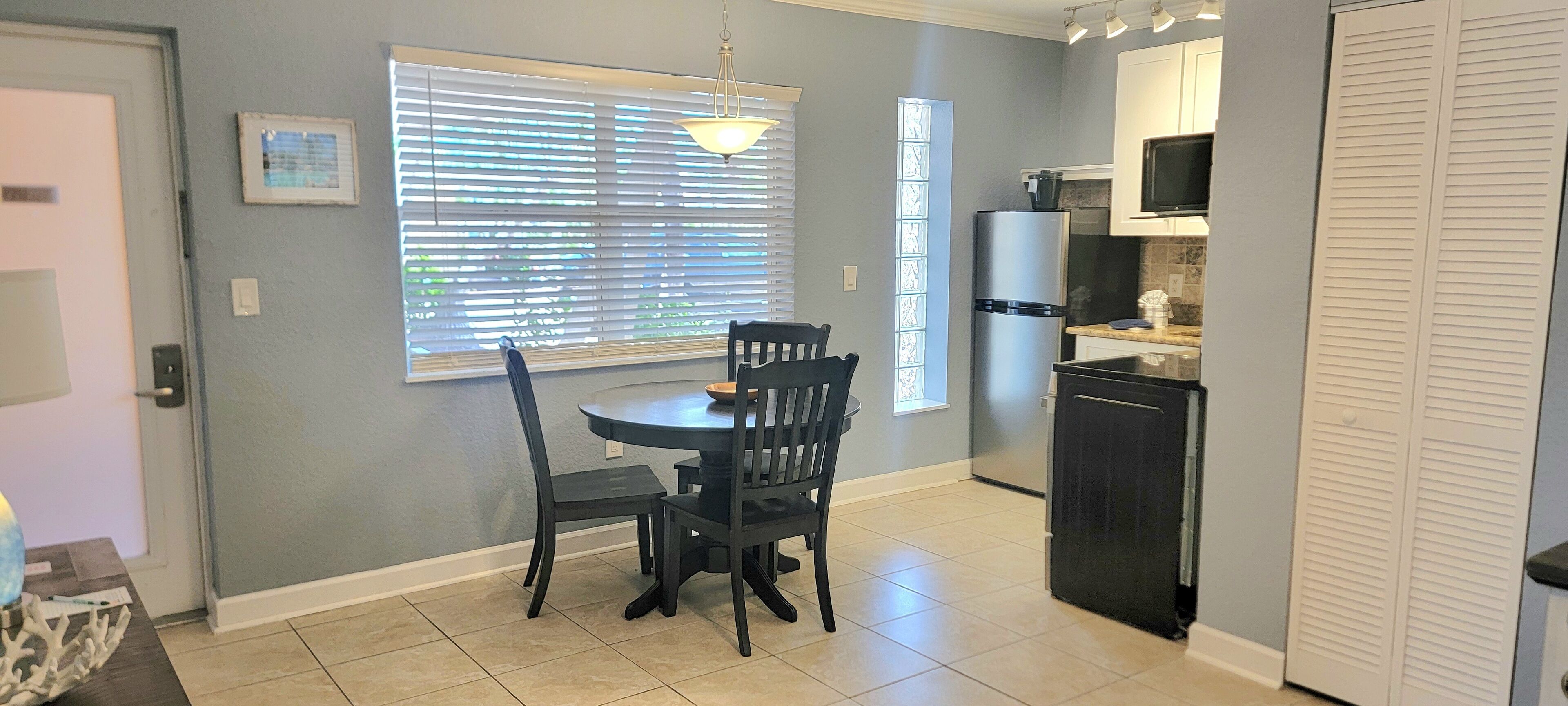 A kitchen with a dining table and chairs, a refrigerator, and a microwave.
