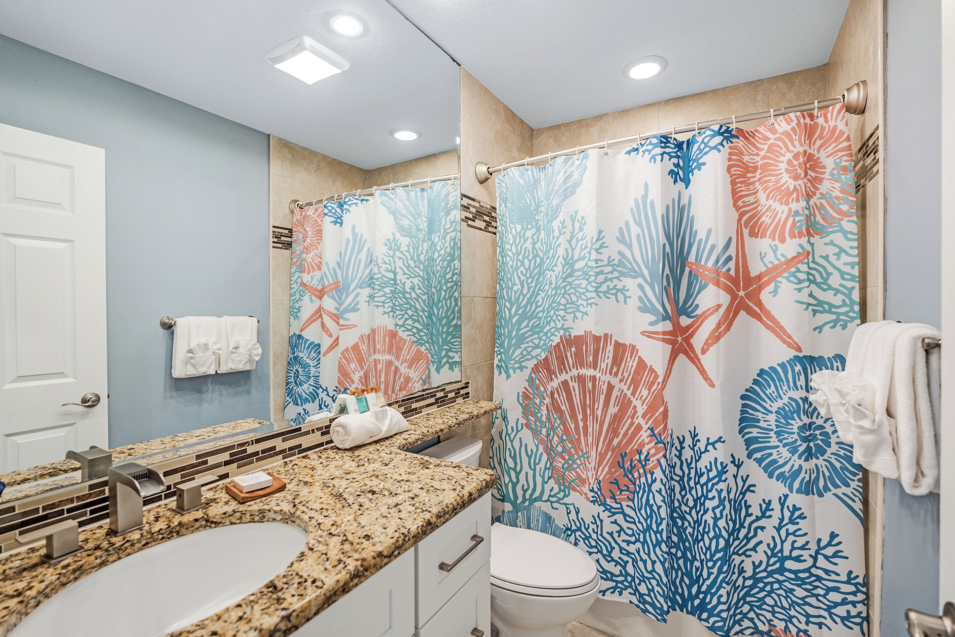 A bathroom with a granite countertop, white sink, and a shower curtain with a coral and starfish design.