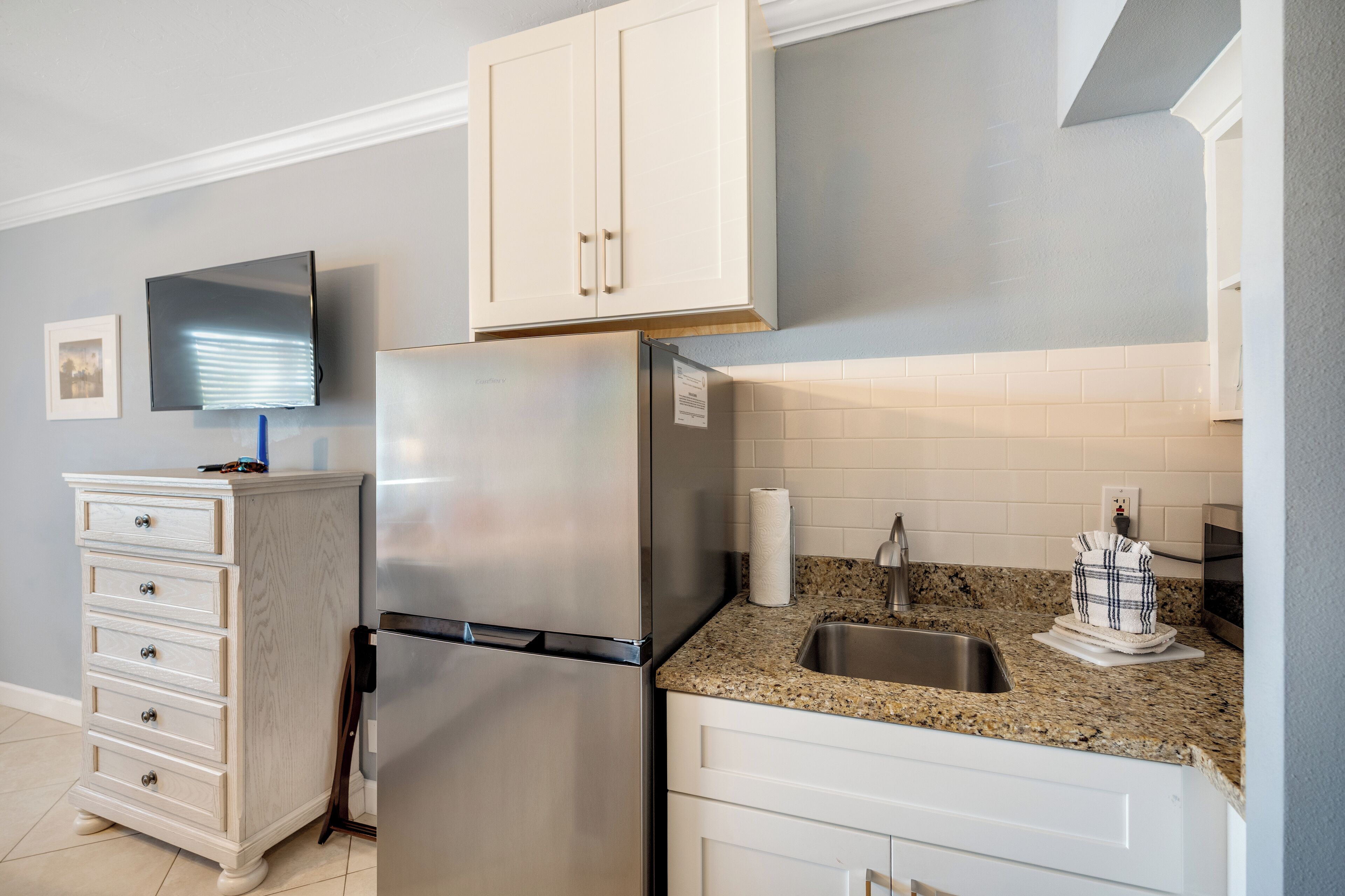 A kitchen with white cabinets, a stainless steel refrigerator, a granite countertop, and a built-in oven.