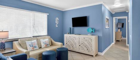 Una sala de estar con un sofá color beige, sillones azules, un aparador blanco y un ventilador de techo.